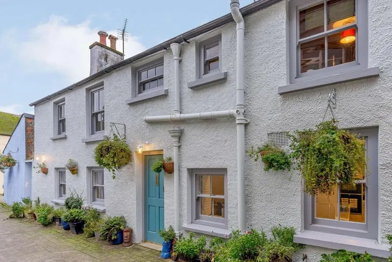 Heritage cottage front with turquoise door and hanging baskets in Tenby