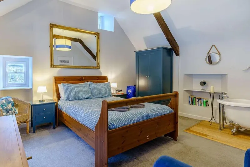 Master bedroom with exposed beams, sleigh bed and roll-top bath in alcove