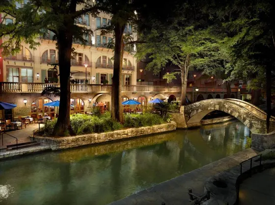 Stone footbridge over a riverwalk with blue umbrellas at night
