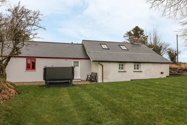 Bwthyn Lan cottage exterior with lawn and hot tub in the garden