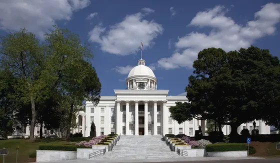 Alabama State Capitol framed by trees beneath a blue sky