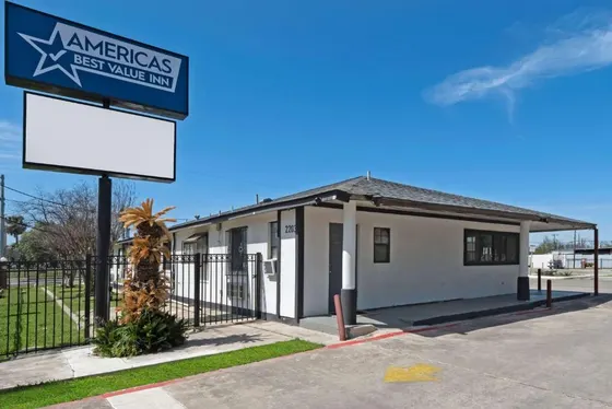 White one-story building with a tall blue sign and palm
