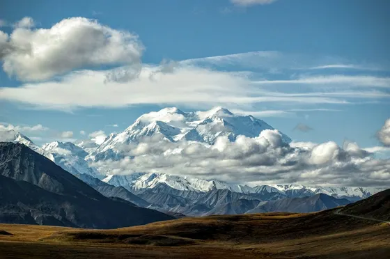 Snowy mountain peak above brown tundra and clouds