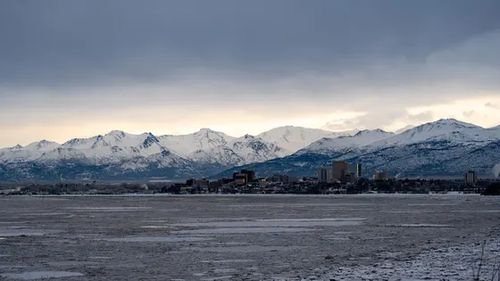 Anchorage skyline across a snowy inlet with the Chugach Mountains behind it