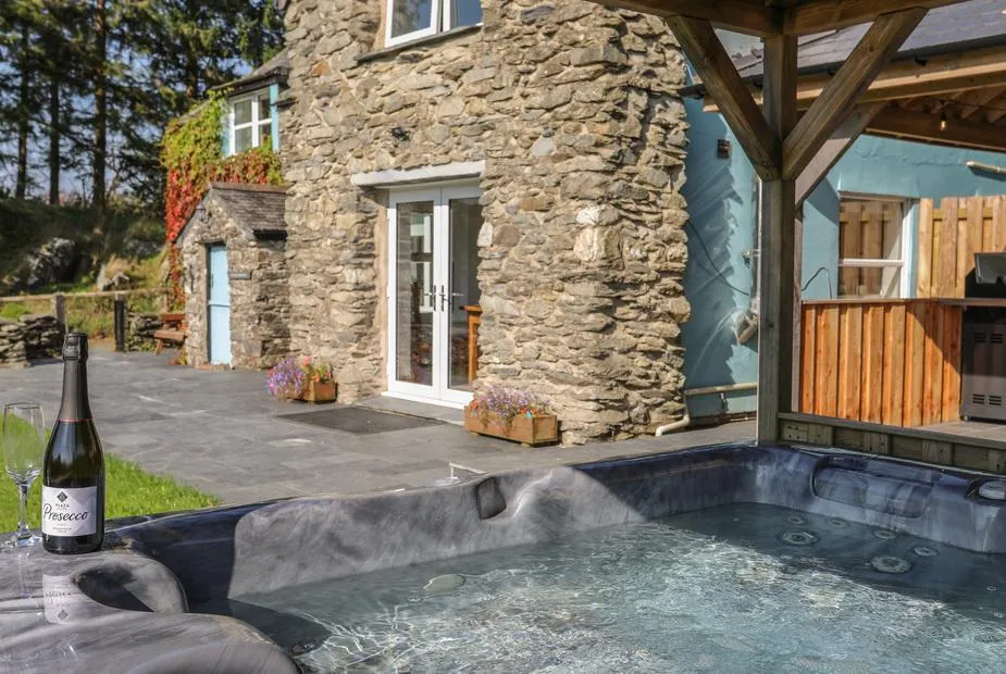 Maes Madog hot tub beside stone cottage and covered outdoor kitchen
