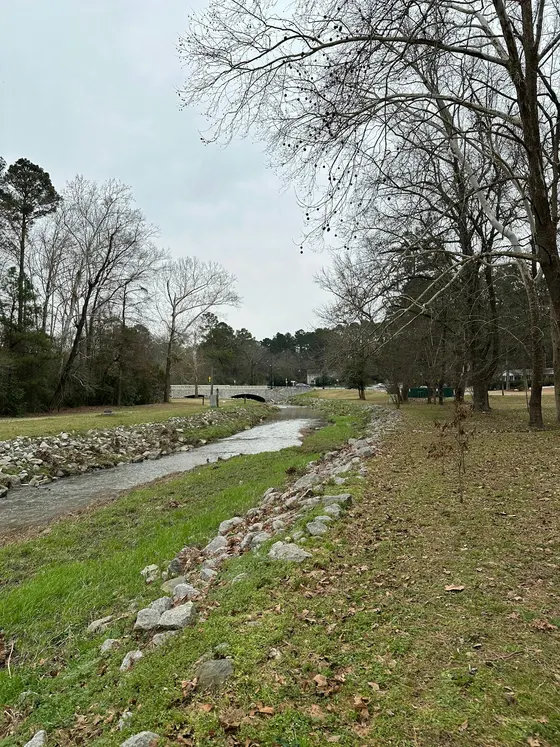 Tree-lined Rae's Creek flowing toward a stone bridge