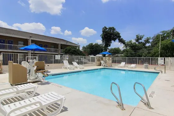 Pool with white lounge chairs in front of blue motel doors
