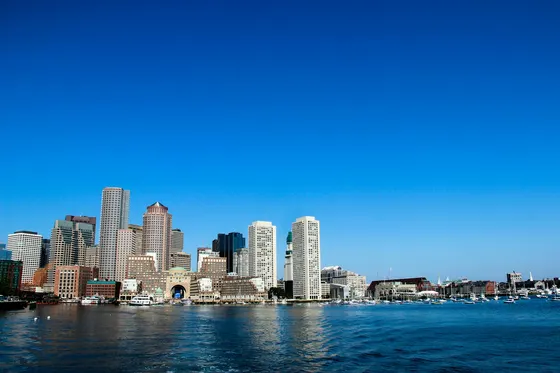 Boston skyline and boats across the harbor under a clear blue sky