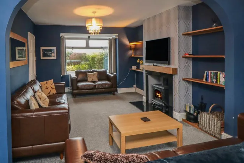 Castle View living room with deep blue walls and lit wood burner