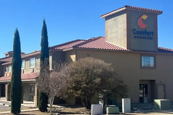 Tan stucco hotel with red tile roofs and tall cypress trees