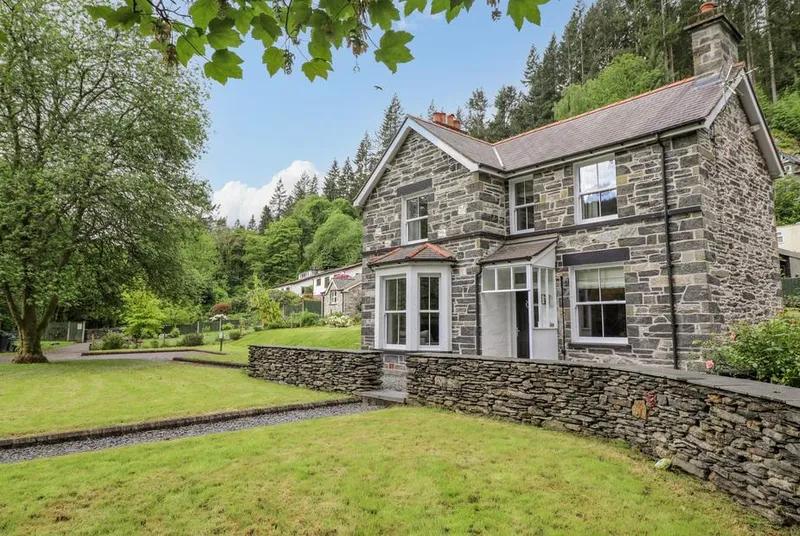 Craigside stone cottage with lawn and woodland backdrop