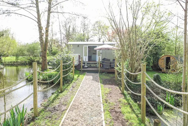Damsel Shepherds Hut from rope-fenced gravel path with deck and barrel sauna