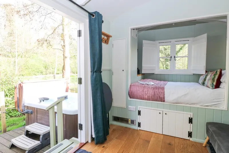 Damsel Shepherds Hut bed nook with hot tub visible through open stable doors