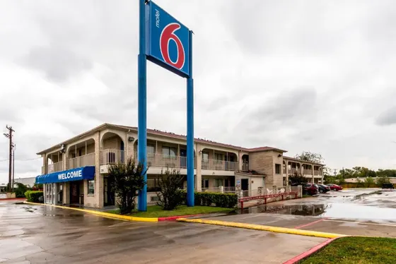 Tan two-story motel with a tall Motel 6 sign and wet parking