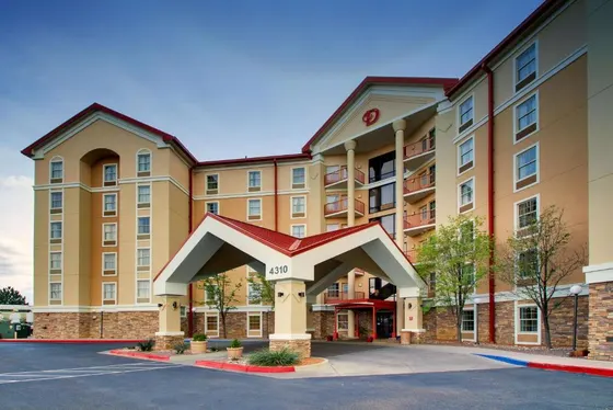 Tan hotel with a white covered entrance and red roof