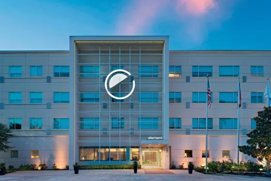 Beige Element hotel at dusk with a glowing circular logo