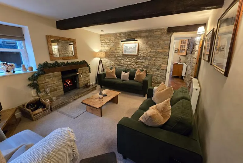 End Cottage living room with exposed stone wall and green velvet sofas