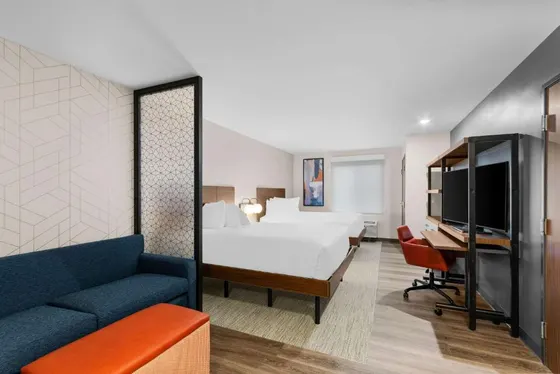 Studio with a blue sofa, orange ottoman, and two beds