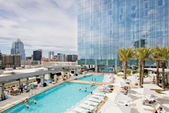 Rooftop pool with lounge chairs below a glass skyscraper