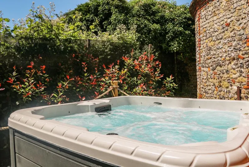 Filbert Pod bubbling hot tub framed by photinia and flint dovecote wall