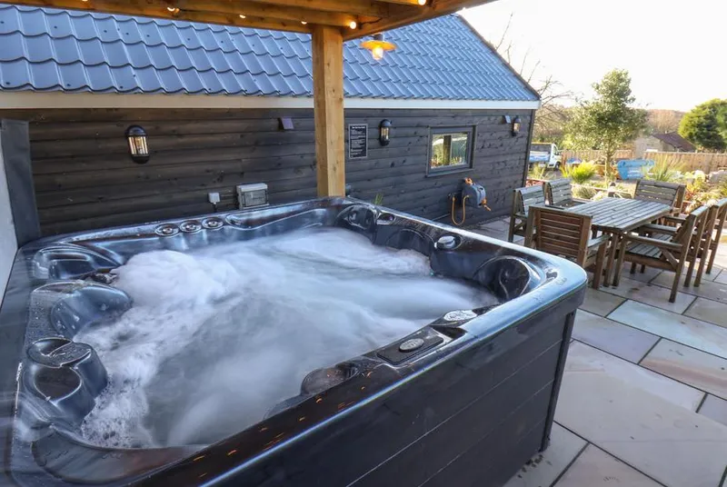 Foxes Den bubbling hot tub under covered pergola with outdoor dining