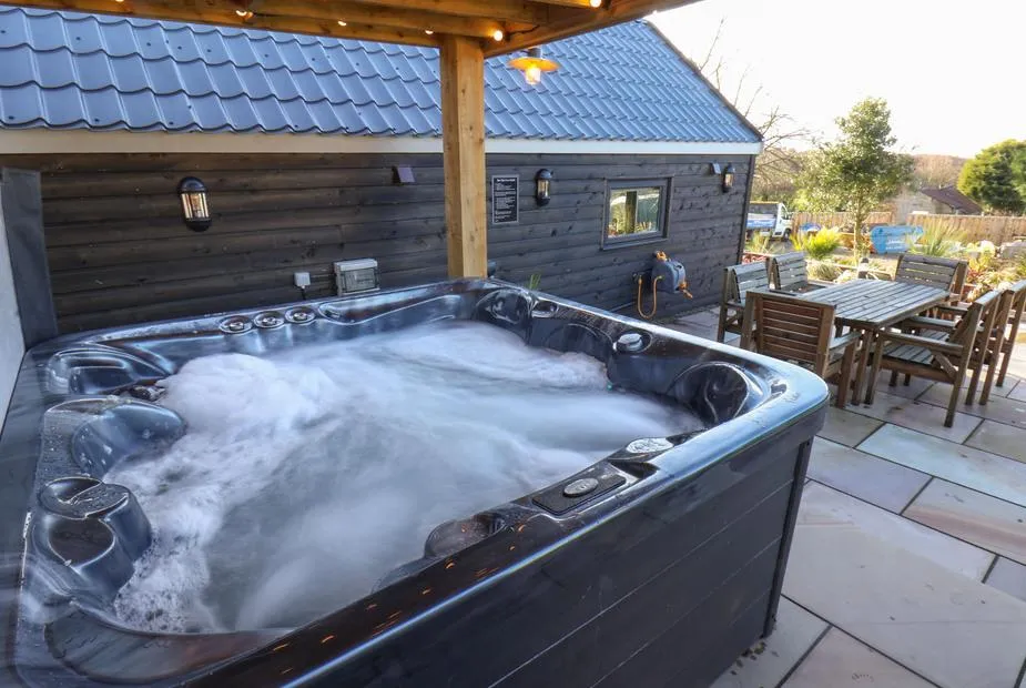 Foxes Den bubbling hot tub under covered pergola with outdoor dining