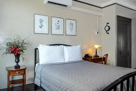 Room with a metal bed, gray quilt, and botanical prints