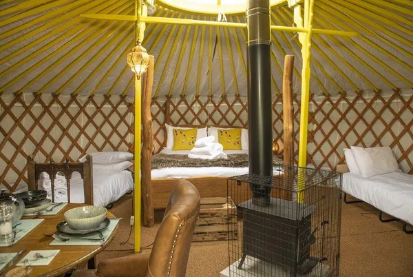 Goldfinch Yurt interior with rustic bed, wood burner and leather sofa