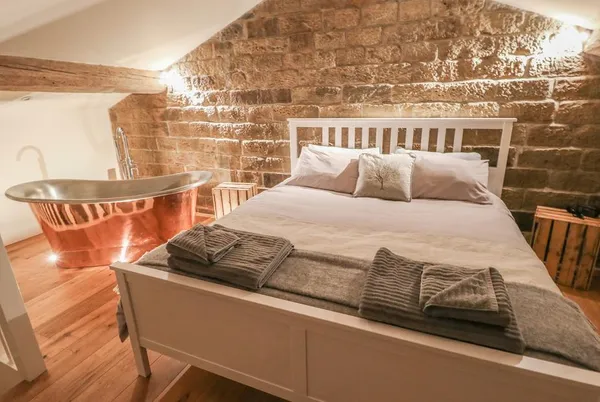 The Stables loft bedroom with copper bath and stone walls in evening light