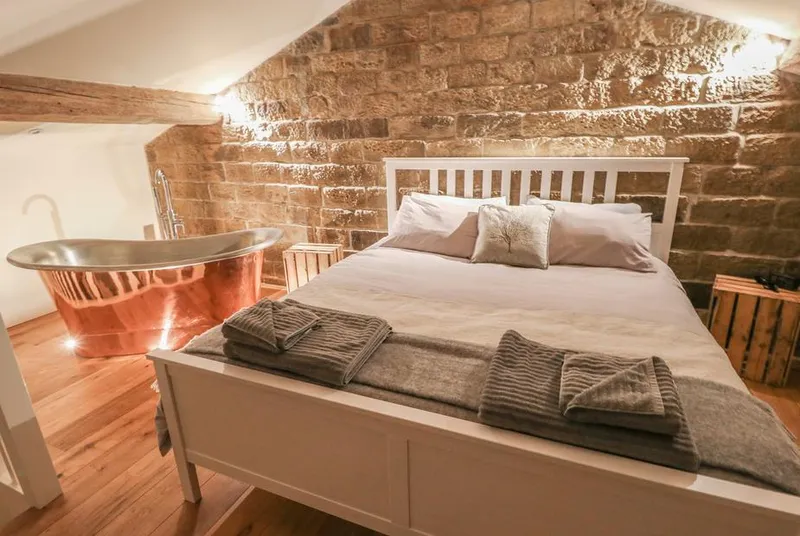 The Stables loft bedroom with copper bath and stone walls in evening light
