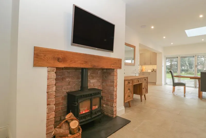 Greenlawns open-plan living area with lit wood burner in brick inglenook