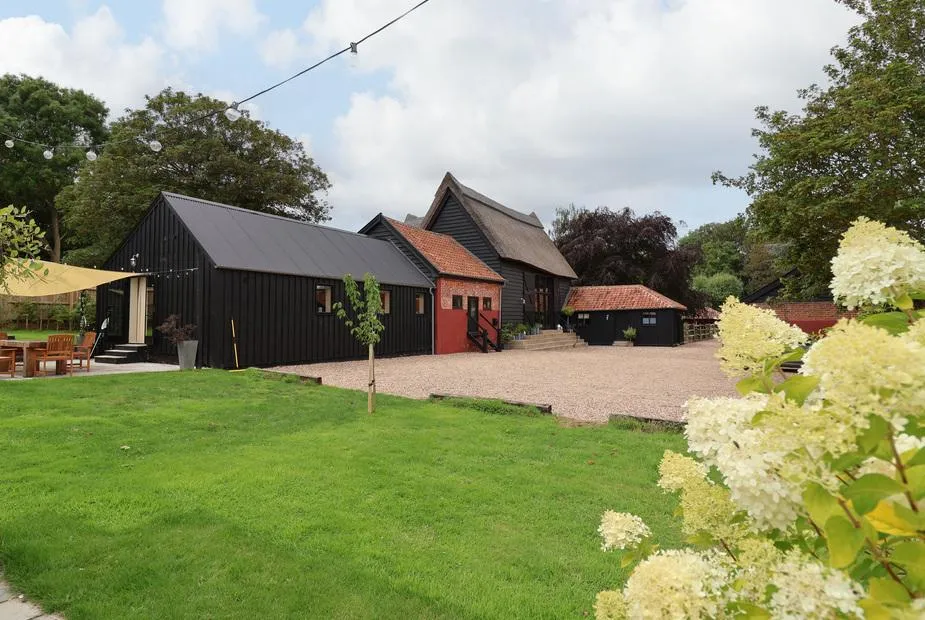 Halcyon Barn black barn complex from garden with green lawn and hydrangeas