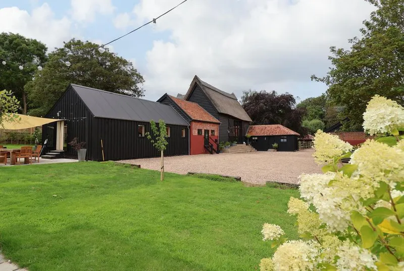 Halcyon Barn black barn complex from garden with green lawn and hydrangeas