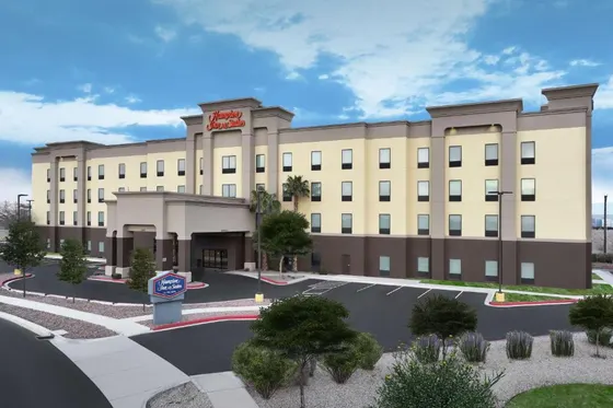 Cream hotel with a Hampton Inn sign over a desert parking lot