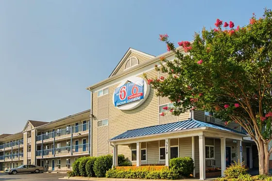 Three-story motel exterior with blue railings and a flowering tree