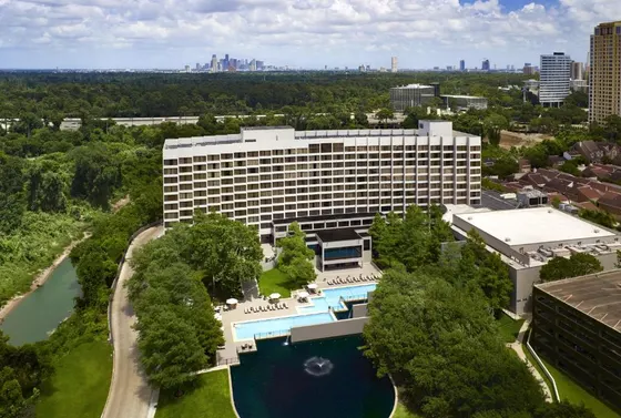 Aerial of a white hotel with a pool, pond, and skyline