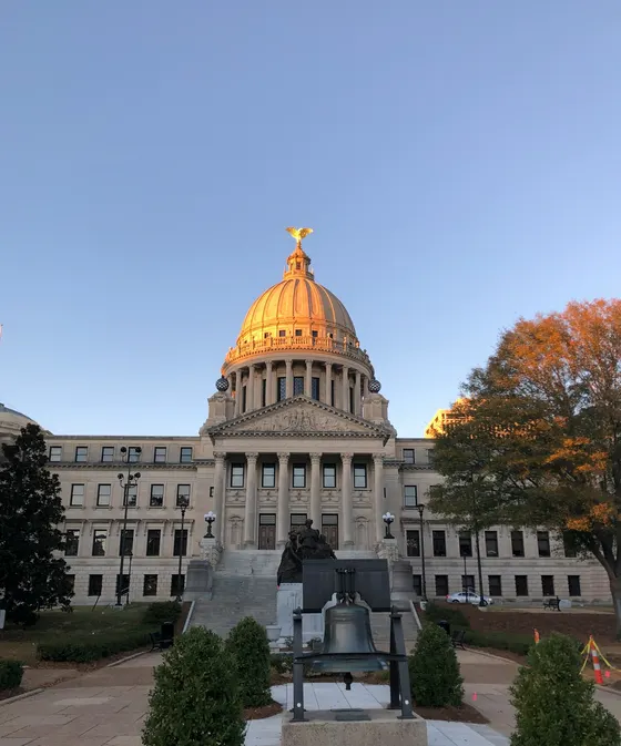 Mississippi State Capitol dome in evening light with a bell in front