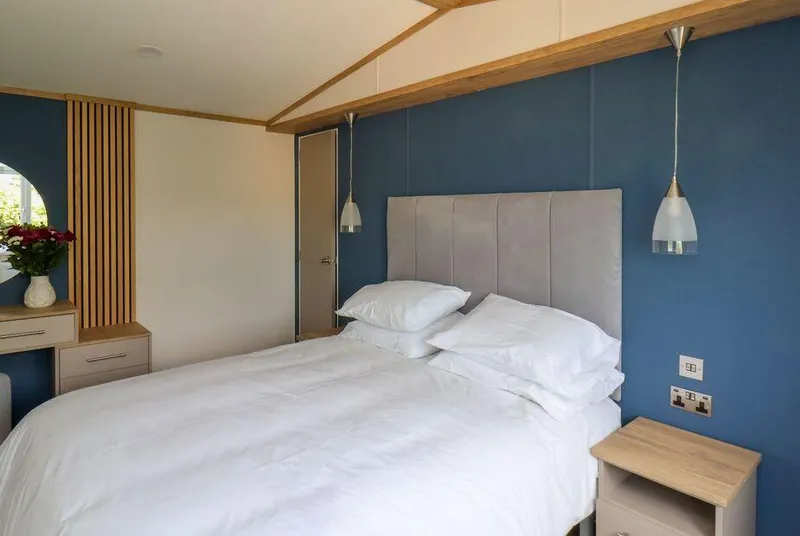 Juniper Lodge master bedroom with blue feature wall, oak beams and pendant lights