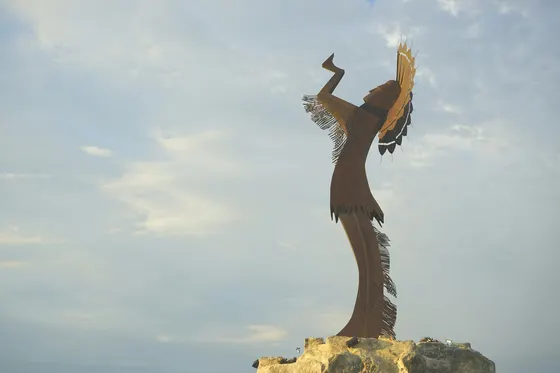 Tall metal statue with raised hands against a cloudy sky