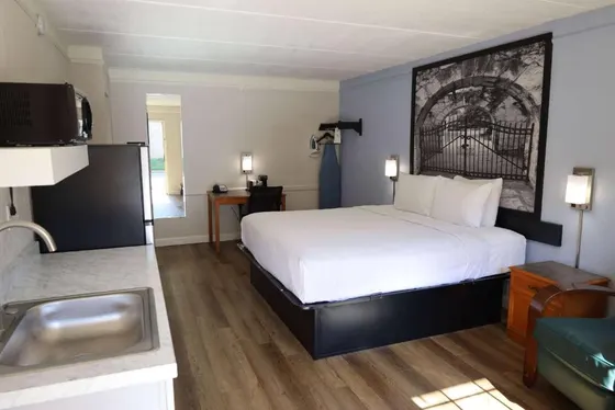 Studio room with a kitchenette, white bed, and wood floors