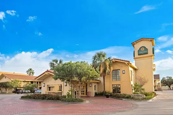 Tan hotel with a La Quinta tower, palms, and a brick driveway