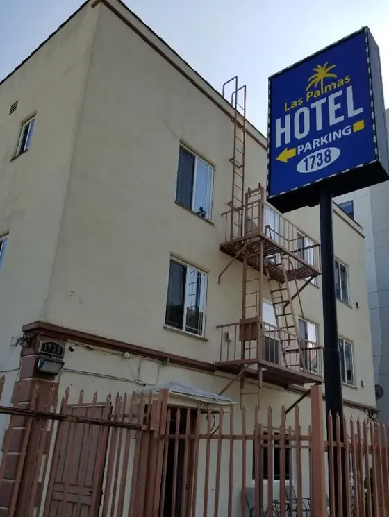 Beige three-story hotel exterior with fire escapes and a blue roadside sign