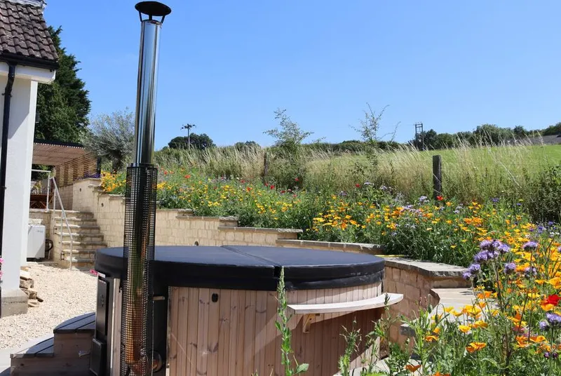 Leafield House wood-fired hot tub with chimney in wildflower garden