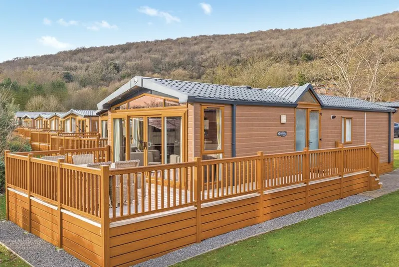 Mendip Premier 2 lodge exterior with wraparound deck and green hillside