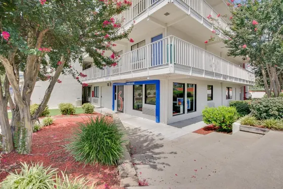 White motel with a blue welcome door and pink tree