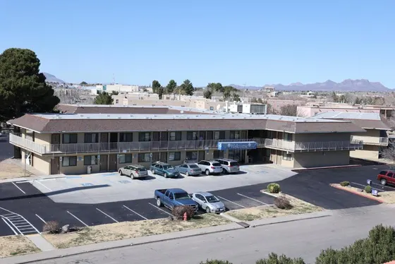 Two-story tan motel with a blue awning and distant mountains