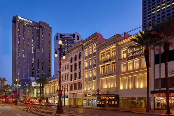 Ornate buildings and a Sheraton tower along streetcar tracks at dusk