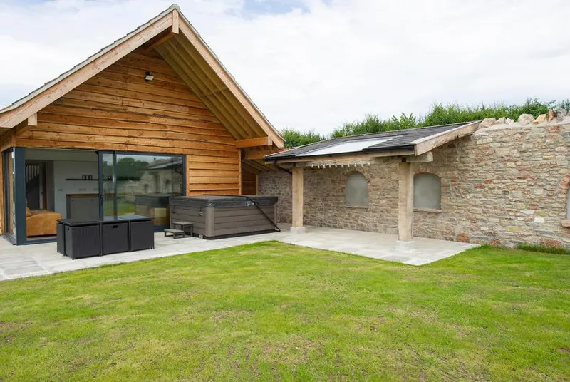 Owl Lodge from lawn with stone wall, hot tub area, and farmland setting