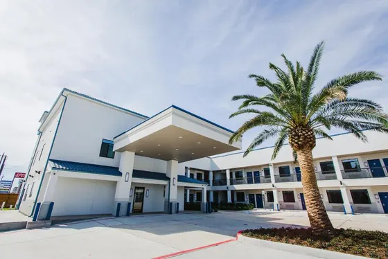 White two-story motel with a palm tree and a large awning