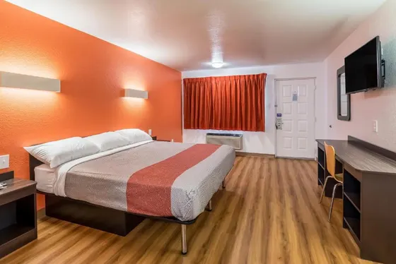 Room with an orange wall, striped comforter, and a wood desk